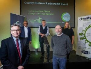 Five people stood in front of a presentation screen which reads County Durham Partnership event, Environment and Climate Change - Our Local Response