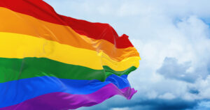 Rainbow flag fluttering in the breeze with cloudy background